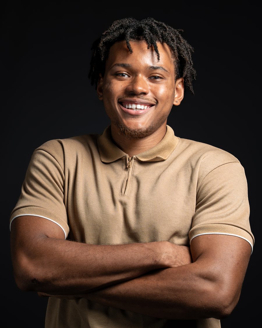 Smiling studio portrait of a young man with arms crossed on a black background